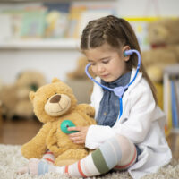 Girl playing doctor with teddy bear.