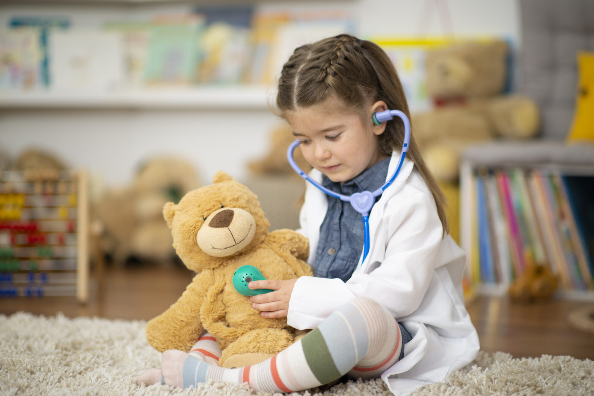 Girl playing doctor with teddy bear.